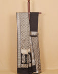 A black and beige patterned saree draped on a wooden hanger against a solid beige background.