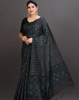 Woman wearing a black saree with green patterns on a gray background
