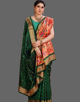 Woman wearing a green and orange paithani saree with a gold border on an orange background