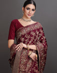 Woman wearing a maroon saree with gold patterns against a gray background