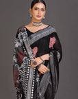 Woman wearing a black saree with white and red patterns on a gray background