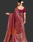 Woman wearing a maroon saree with intricate patterns on an orange background