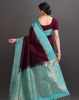 Woman wearing a maroon saree with a turquoise border against a gray background