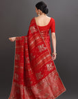 Woman wearing a red saree with intricate patterns on a gray background