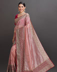 Woman wearing a traditional pink saree with intricate patterns on a gray background