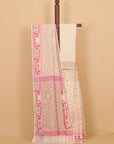 A cream-colored cotton saree with pink and green geometric patterns and a matching cream blouse, draped over a wooden hanger against a solid beige background.