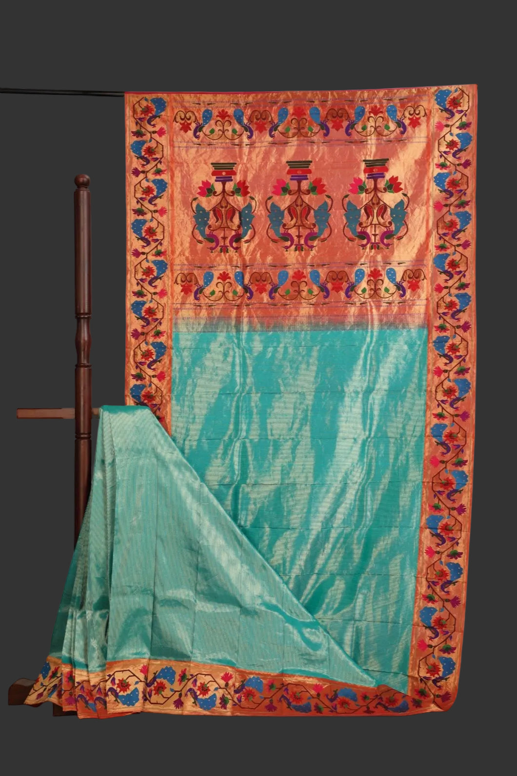 Traditional saree with a colorful border draped over a wooden stand on a white background