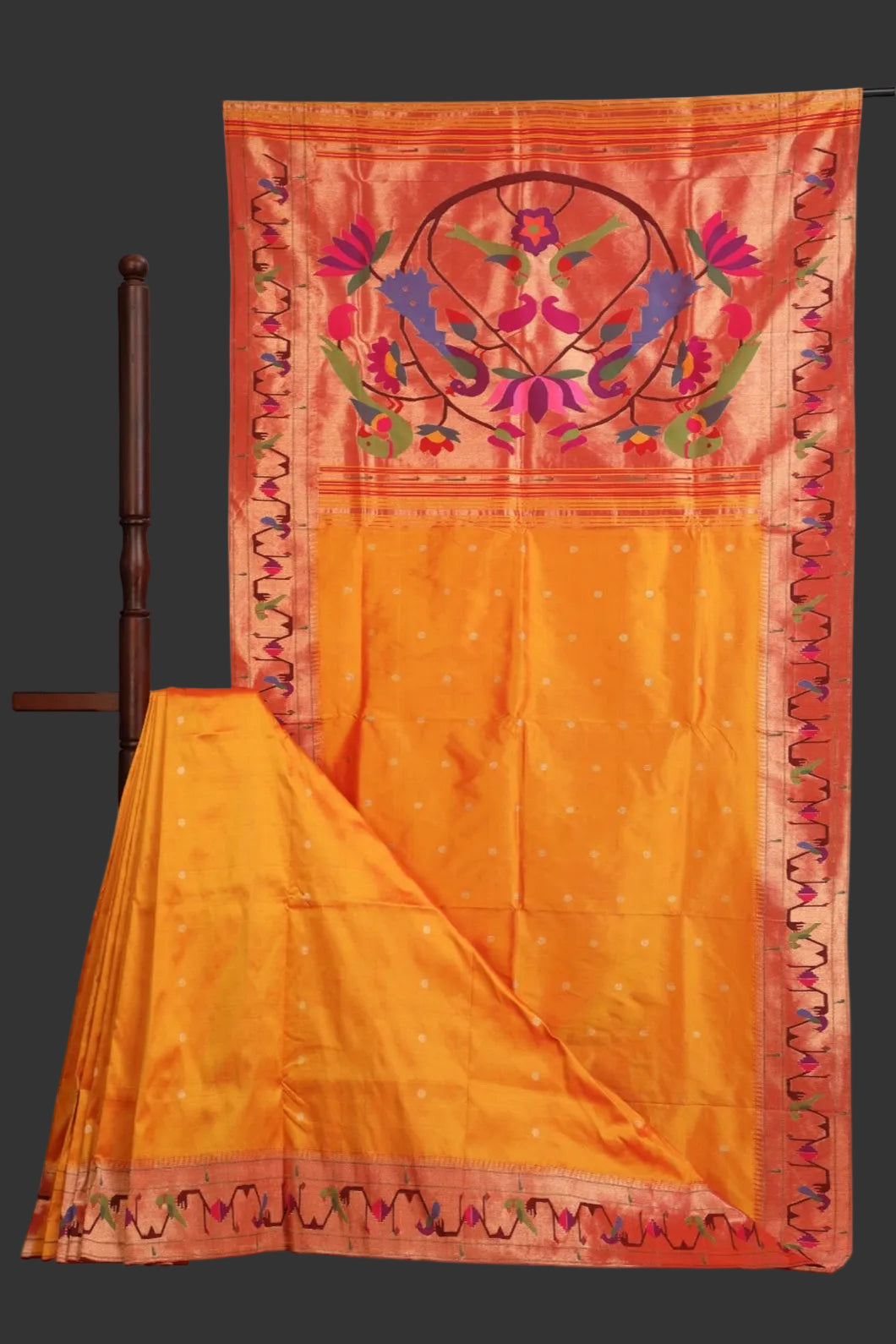 Orange saree with pink border and floral embroidery on a wooden stand.