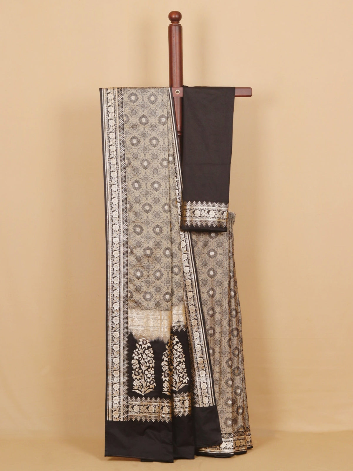 A black and beige patterned saree draped on a wooden hanger against a solid beige background.