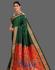 Woman wearing a green and red paithani saree with floral patterns on an orange background