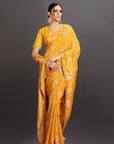 Woman wearing a mustard yellow saree with intricate patterns on a dark background