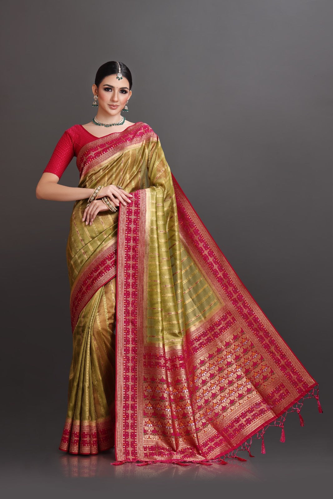 Woman wearing a traditional saree with red and gold patterns on a gray background