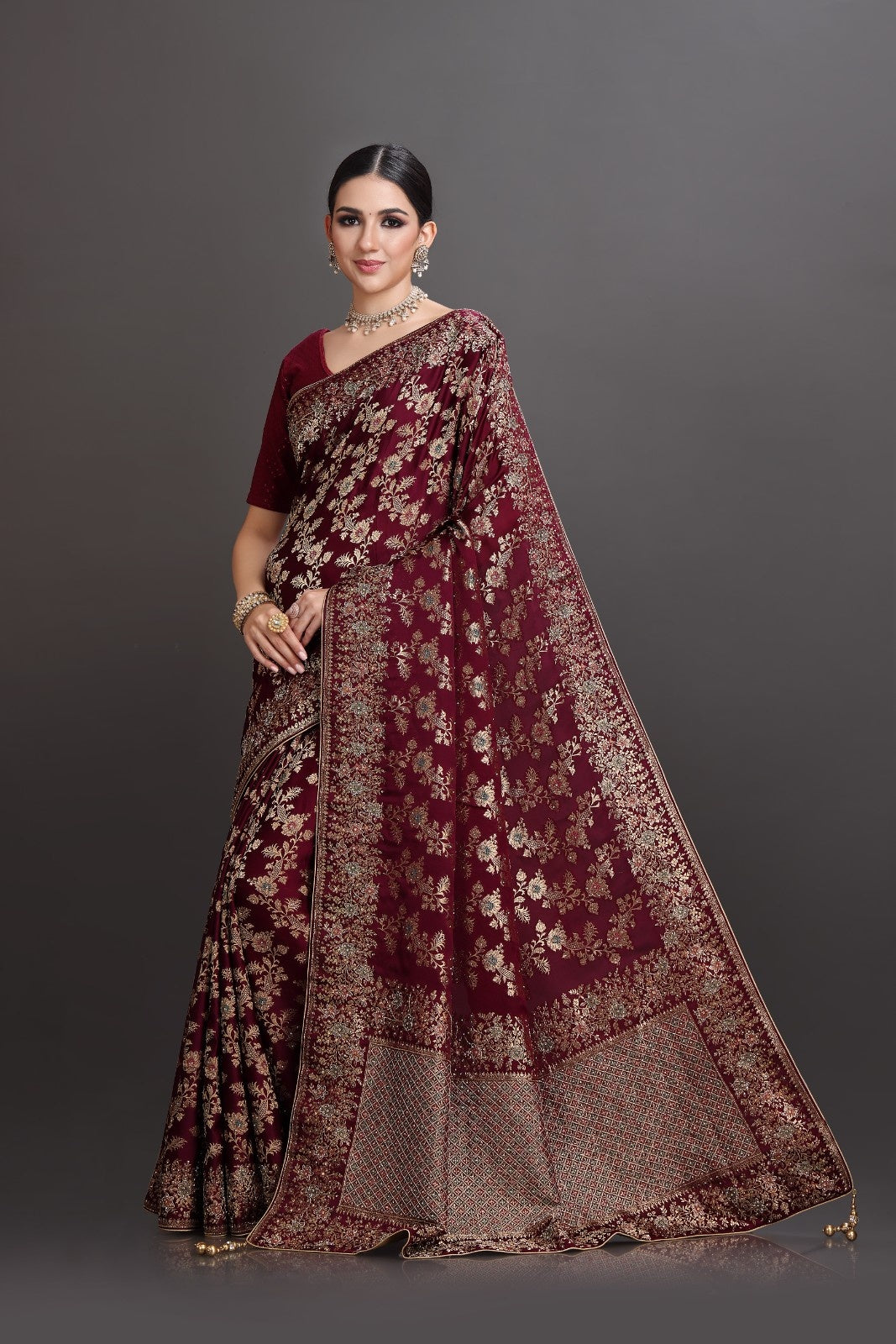 Woman wearing a maroon saree with floral patterns on a gray background