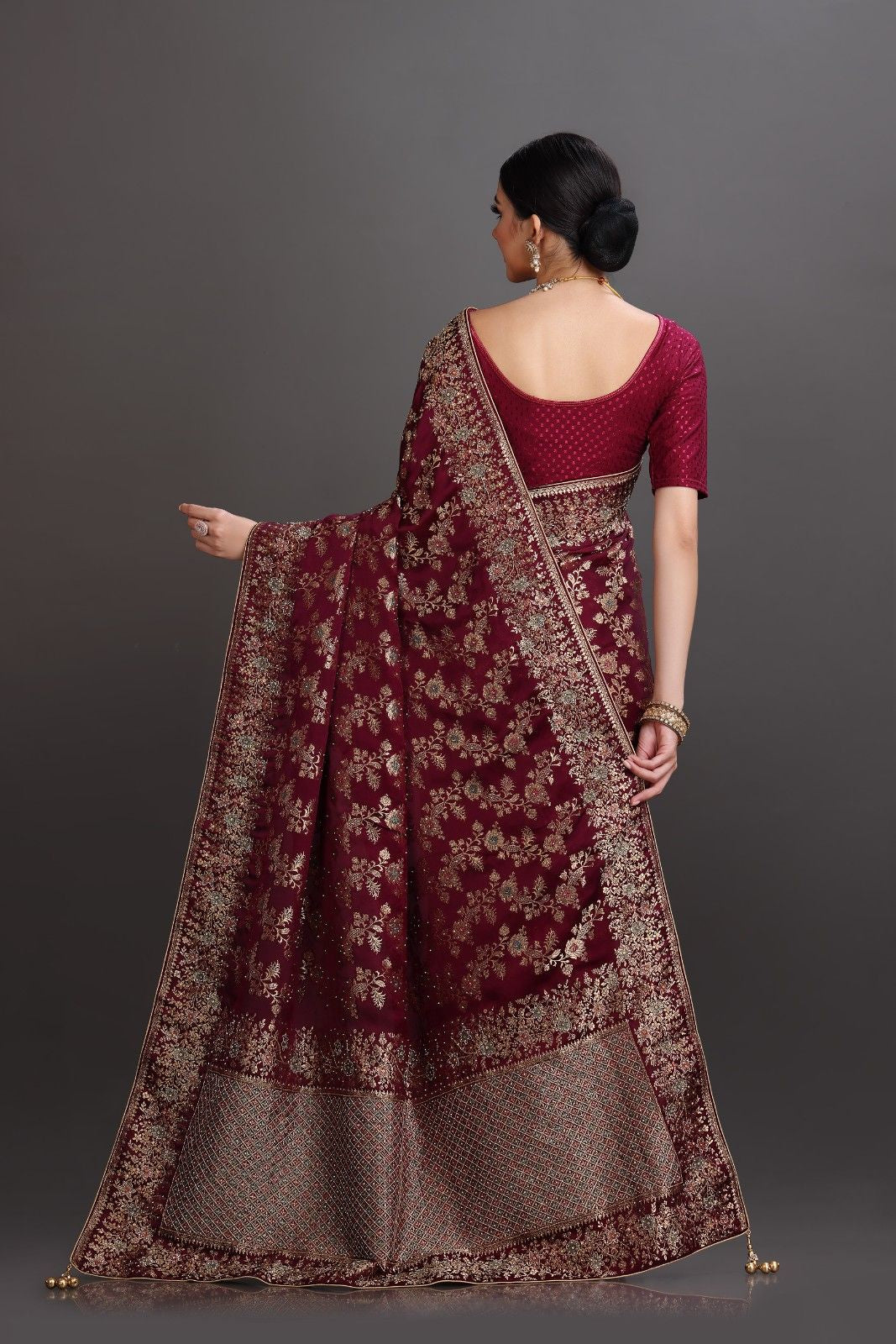 Woman wearing a traditional maroon and gray saree with a plain background