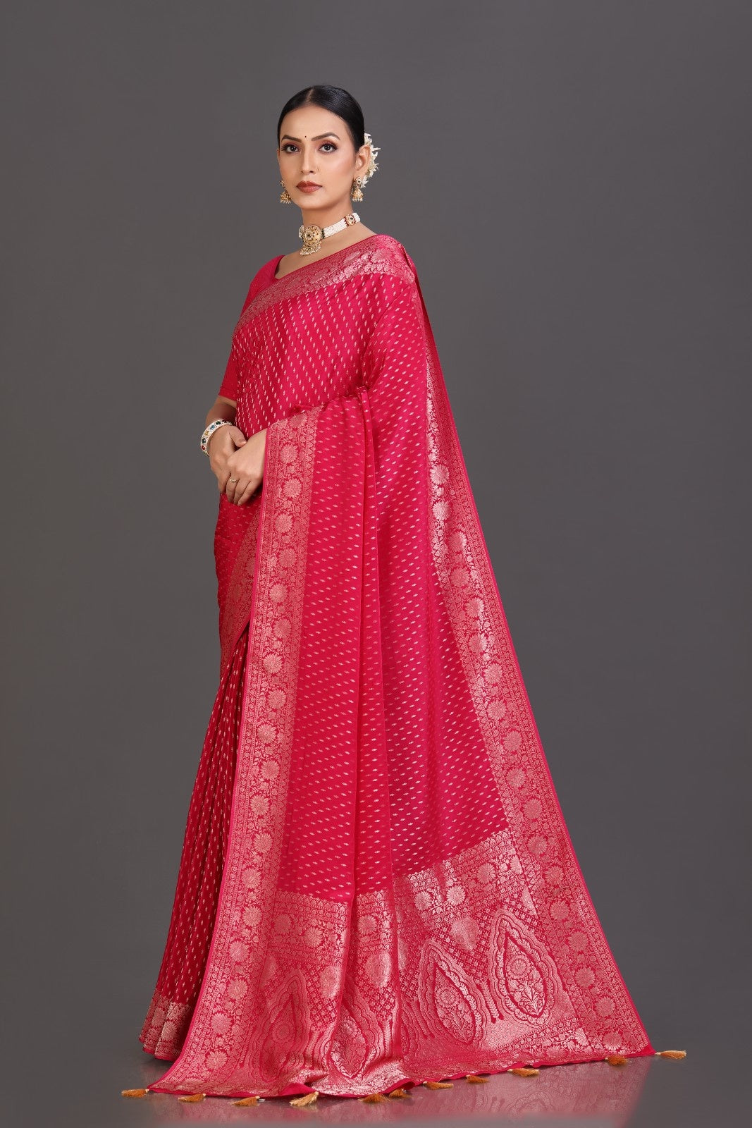 Woman wearing a red saree with intricate patterns on a gray background