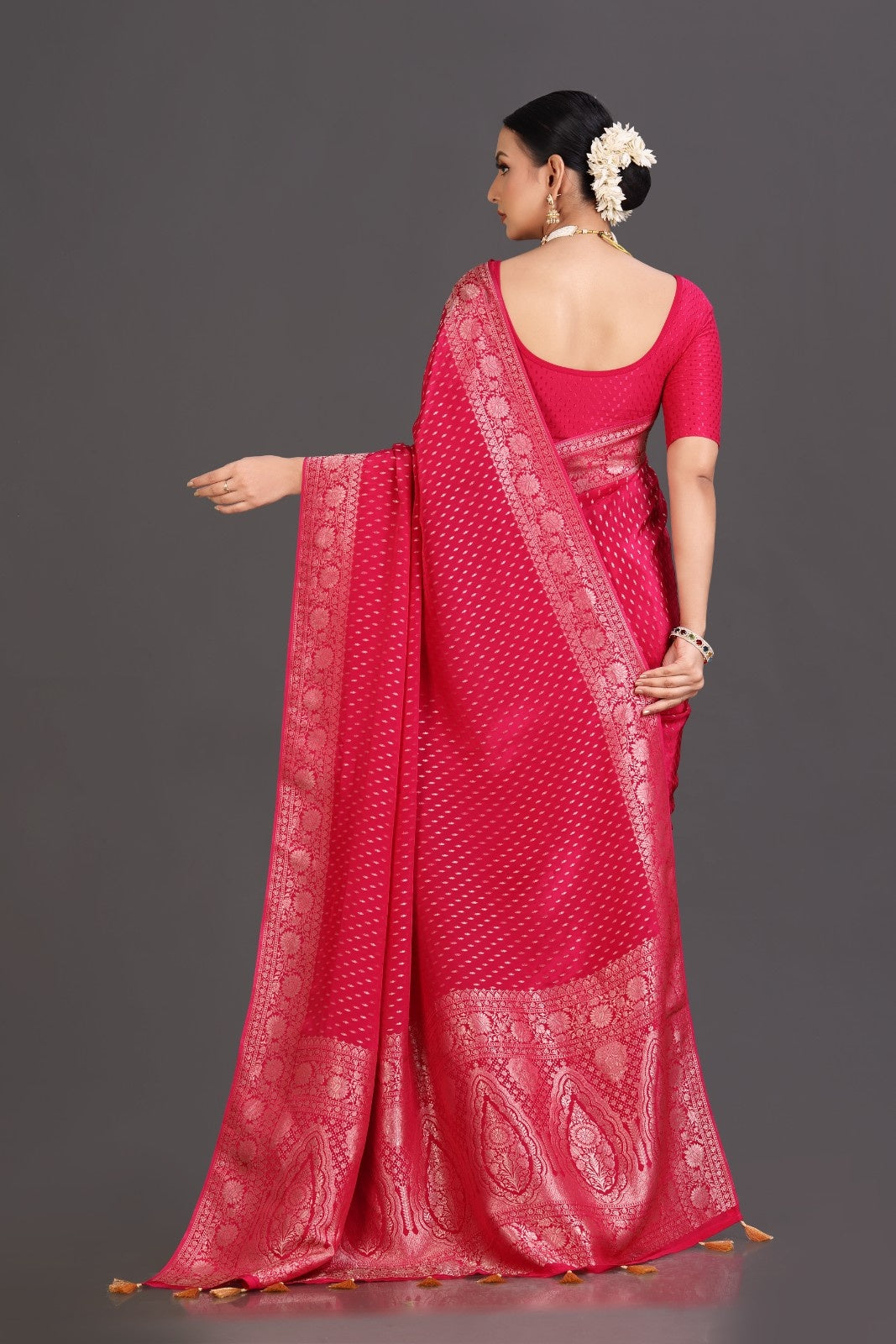 Woman wearing a bright pink saree with white patterns on a gray background