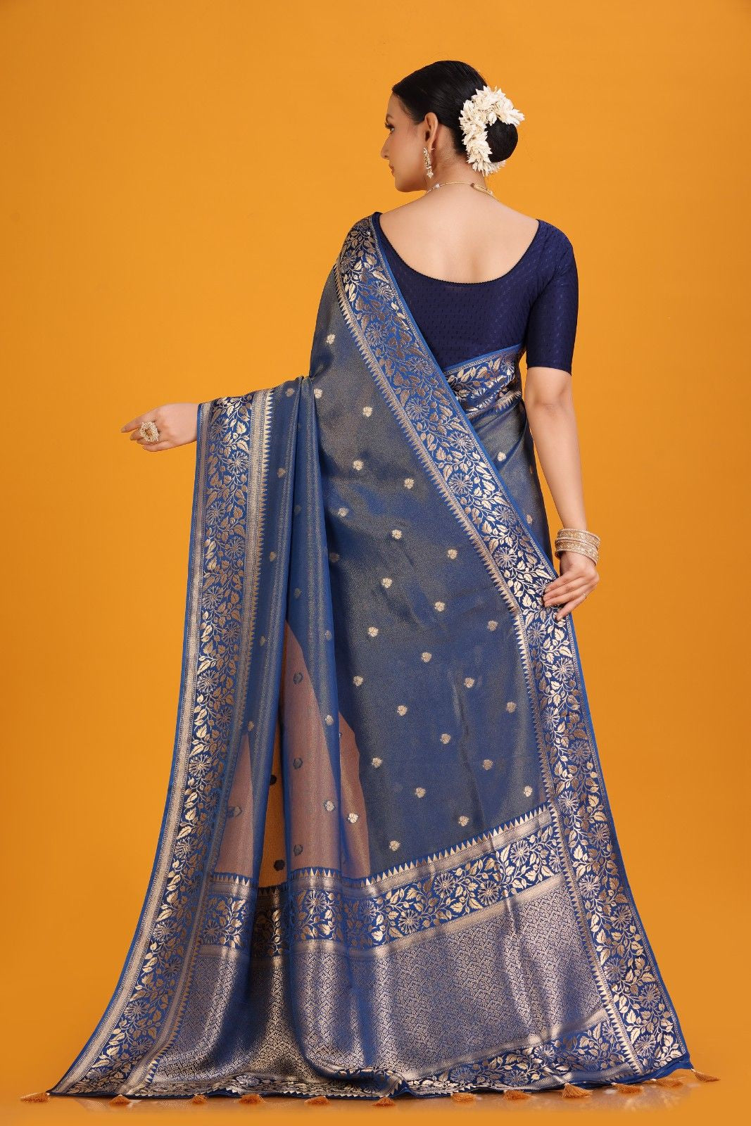 Woman wearing a blue saree with intricate patterns on an orange background