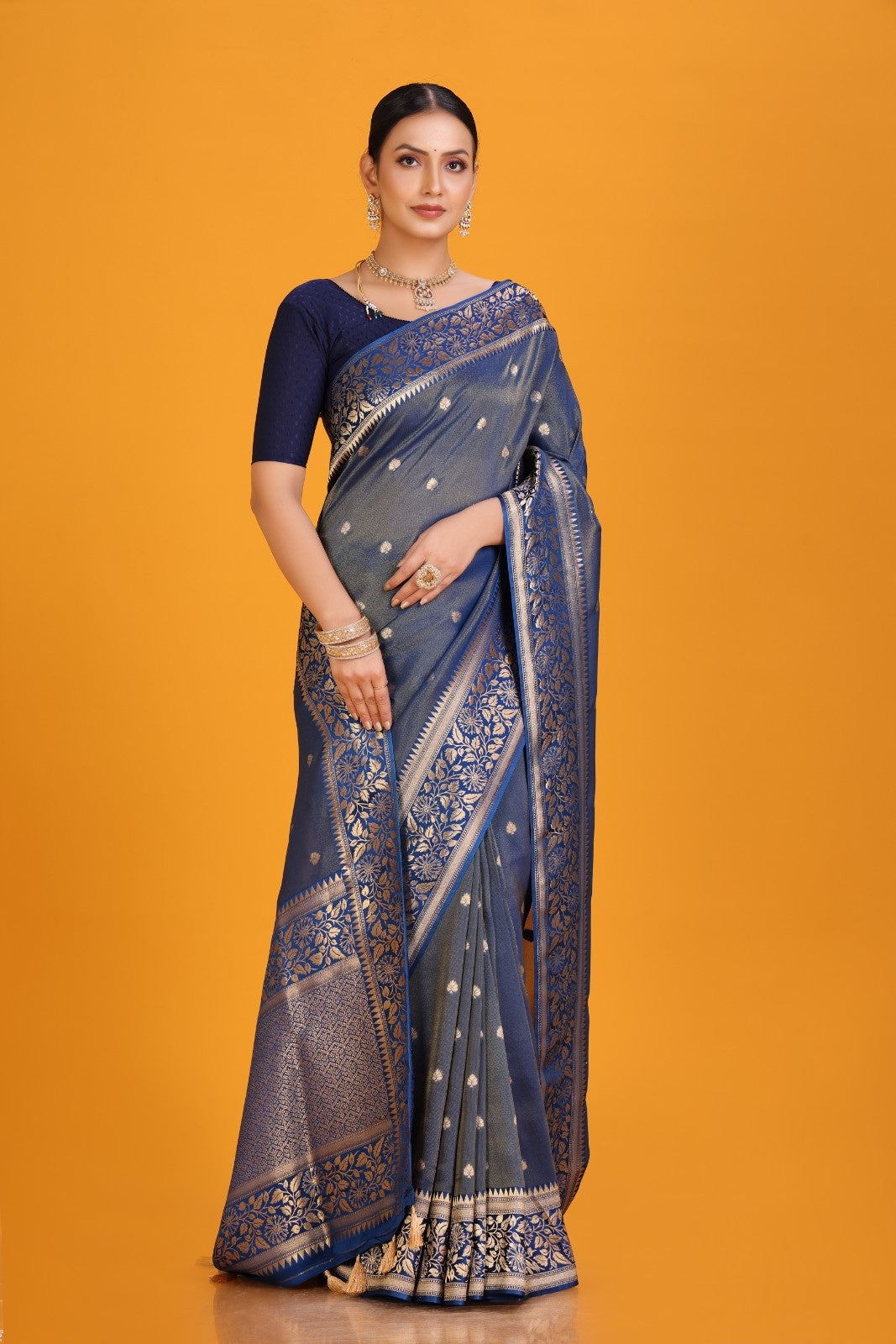 Woman wearing a blue saree with a gold border on an orange background