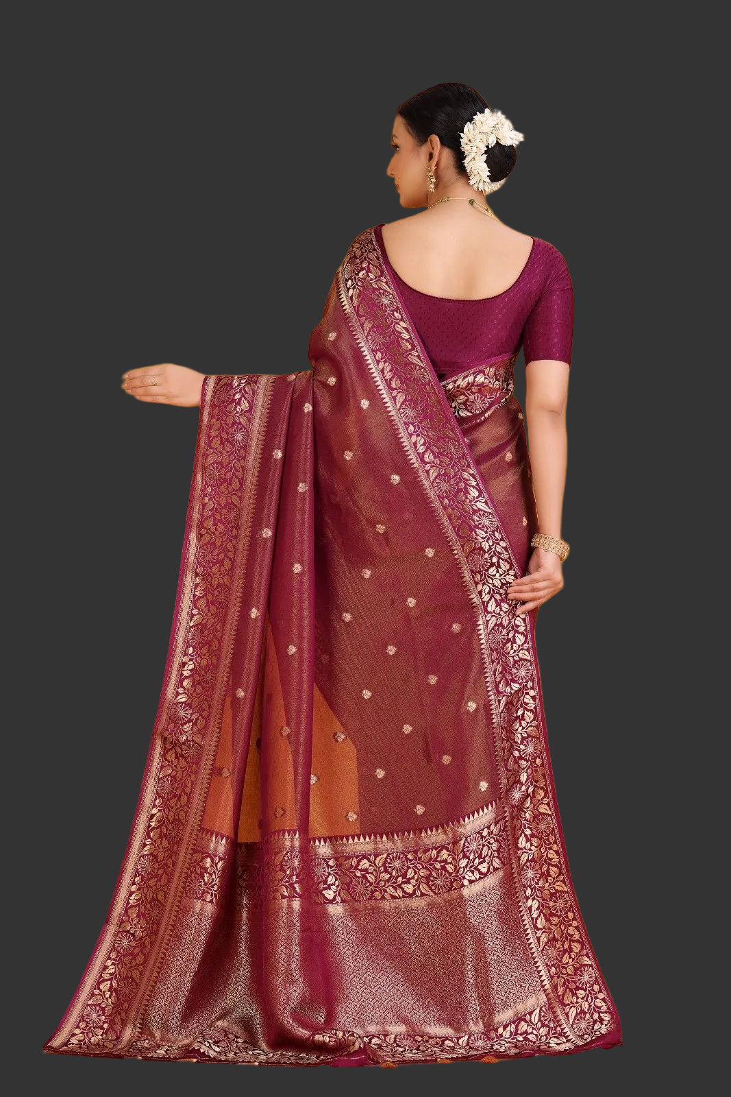 Woman wearing a maroon saree with intricate patterns on an orange background