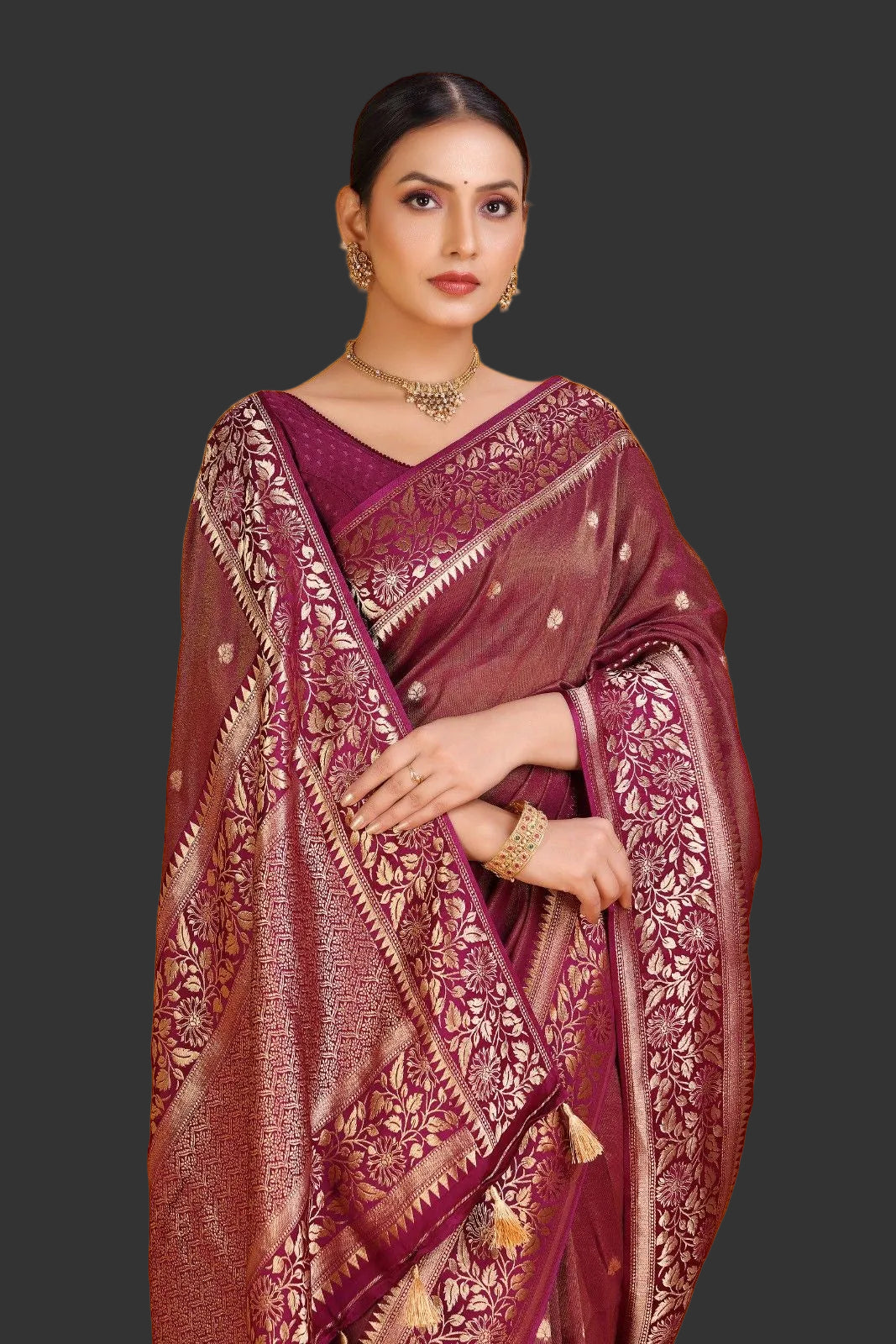 Woman wearing a maroon saree with gold patterns on an orange background