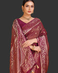 Woman wearing a maroon saree with gold patterns on an orange background