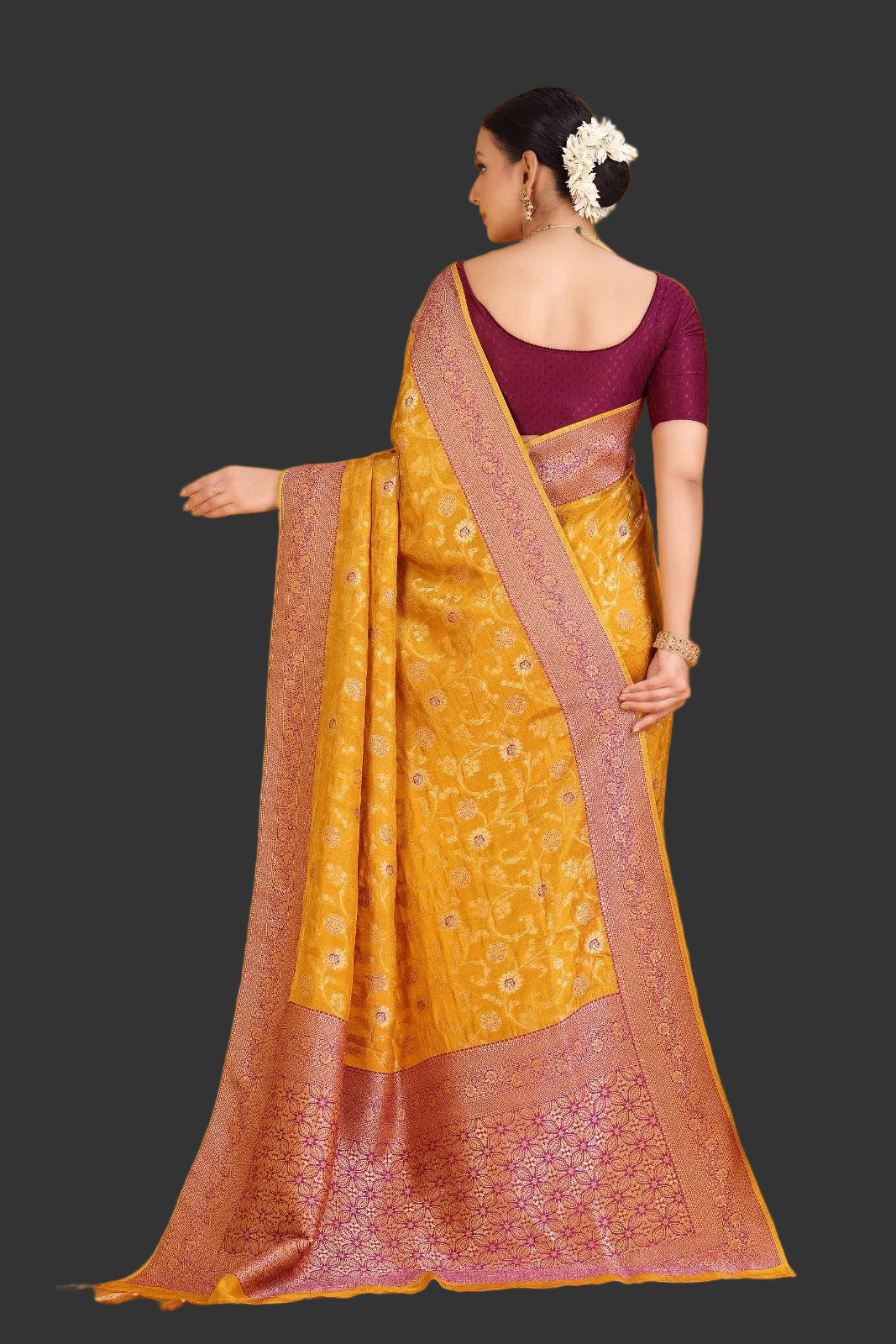 Woman wearing a yellow saree with a maroon blouse against an orange background