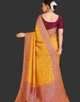 Woman wearing a yellow saree with a maroon blouse against an orange background