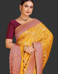 Woman wearing a yellow saree with pink border on an orange background