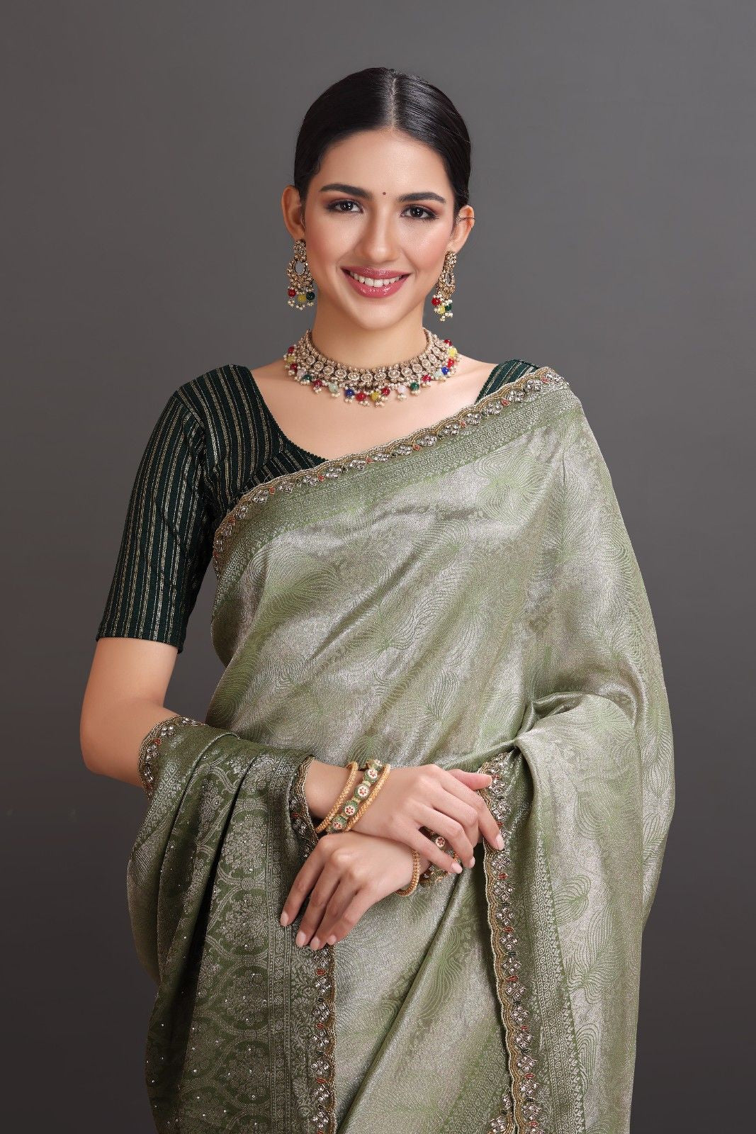 Woman wearing a green saree with jewelry against a gray background