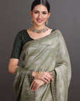 Woman wearing a green saree with jewelry against a gray background