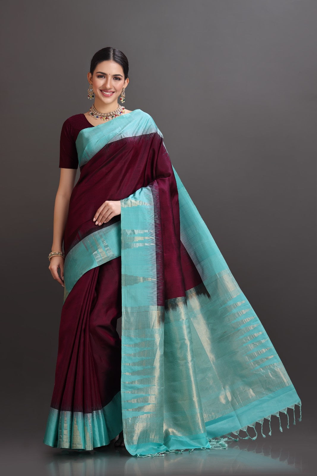 Woman wearing a maroon and turquoise saree on a gray background