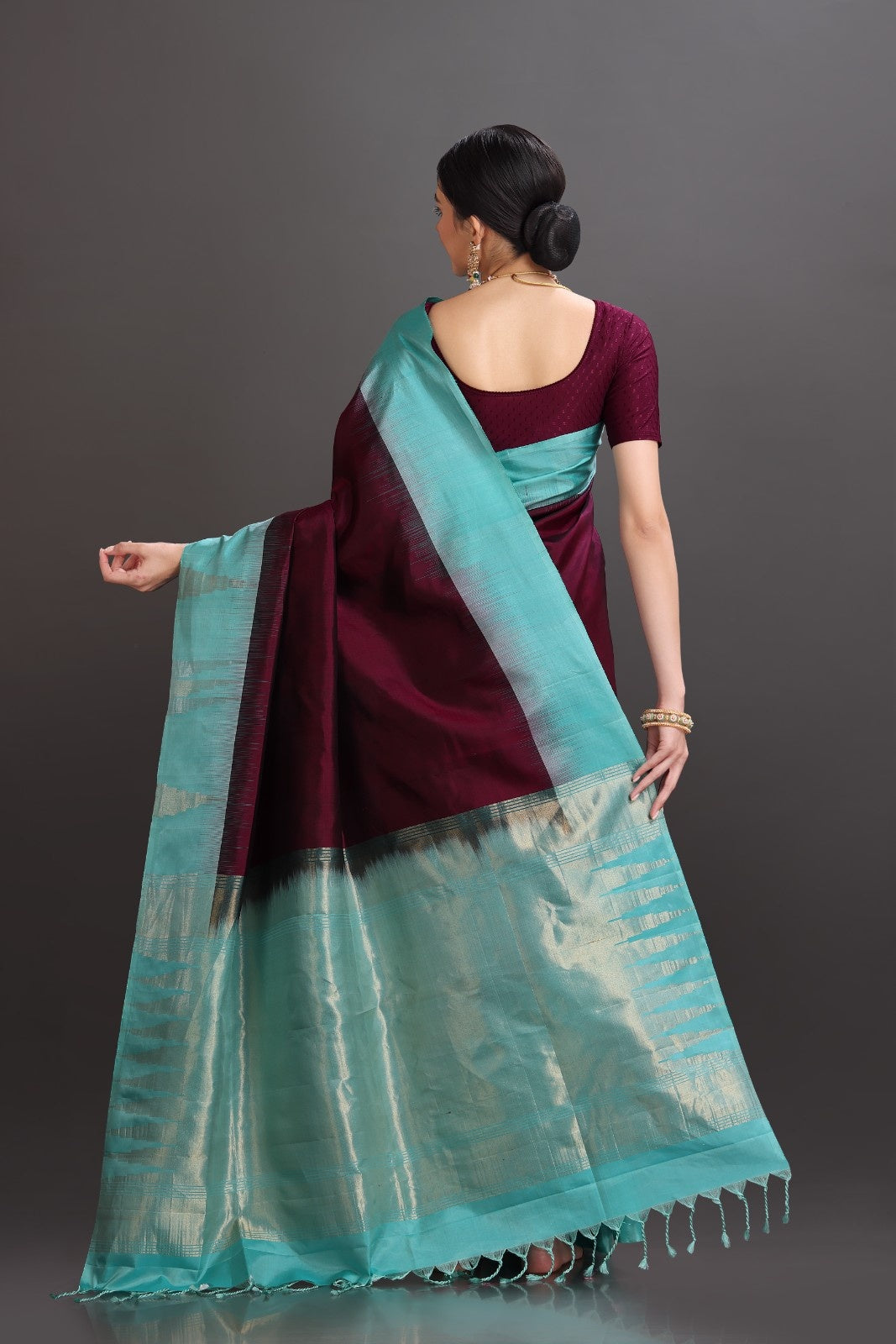 Woman wearing a maroon saree with a turquoise border against a gray background