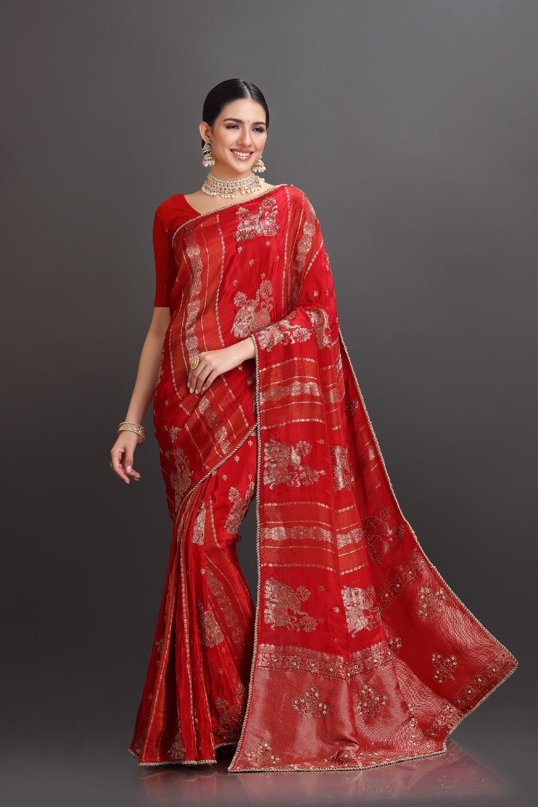 Woman wearing a red saree with gold patterns on a gray background