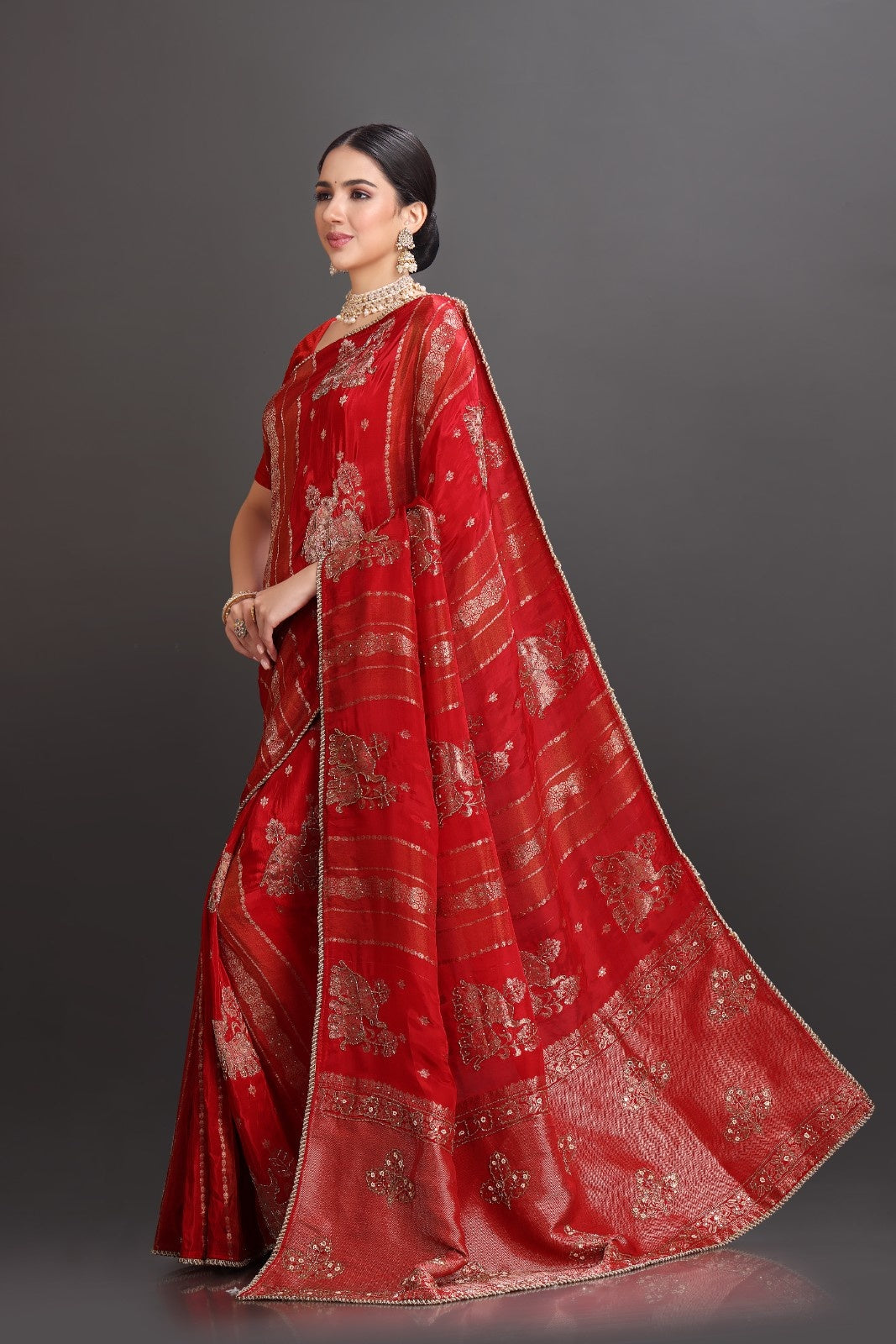 Woman wearing a red saree with gold patterns on a dark background