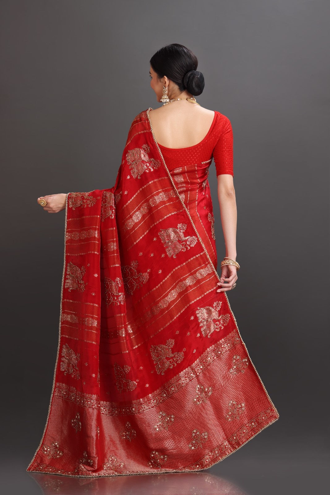Woman wearing a red saree with intricate patterns on a gray background