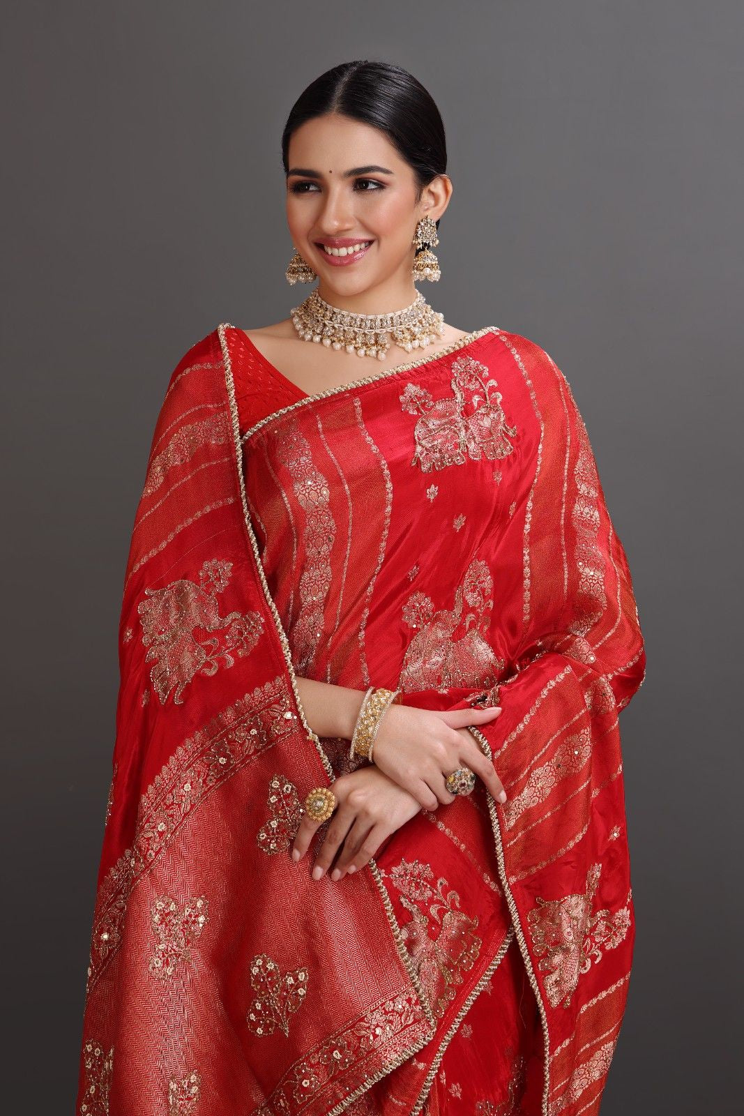 Woman wearing a red saree with gold embroidery against a gray background