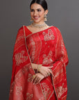 Woman wearing a red saree with gold embroidery against a gray background