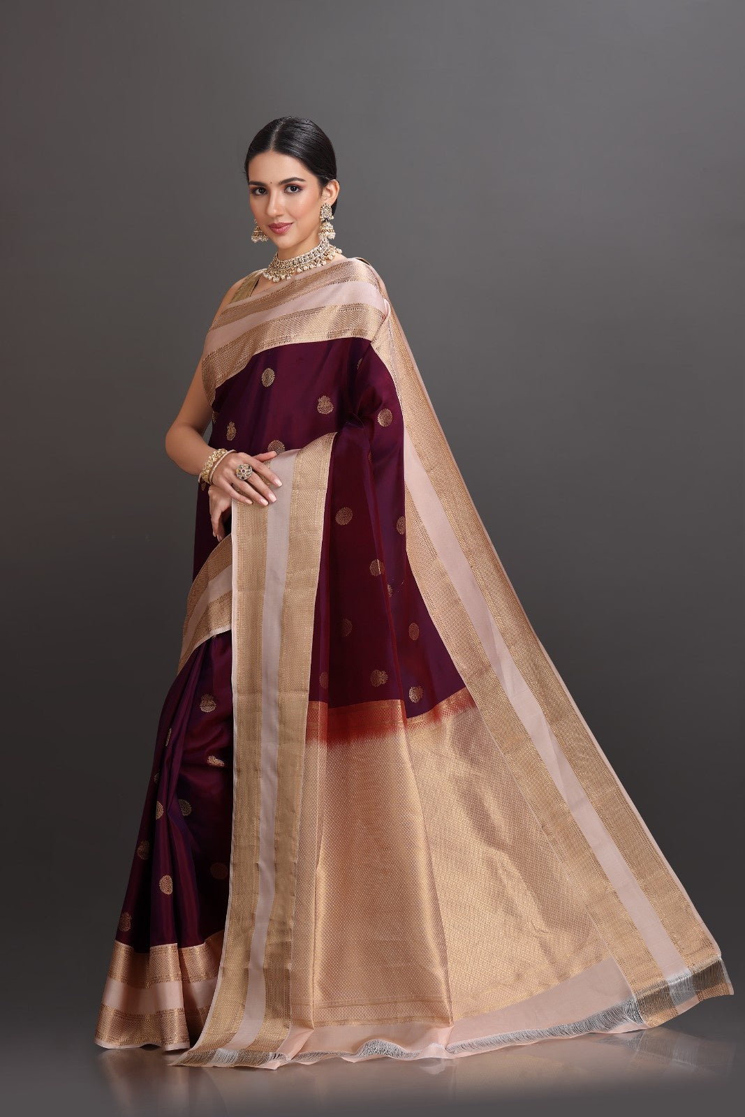 Woman wearing a traditional maroon and beige saree with a plain background