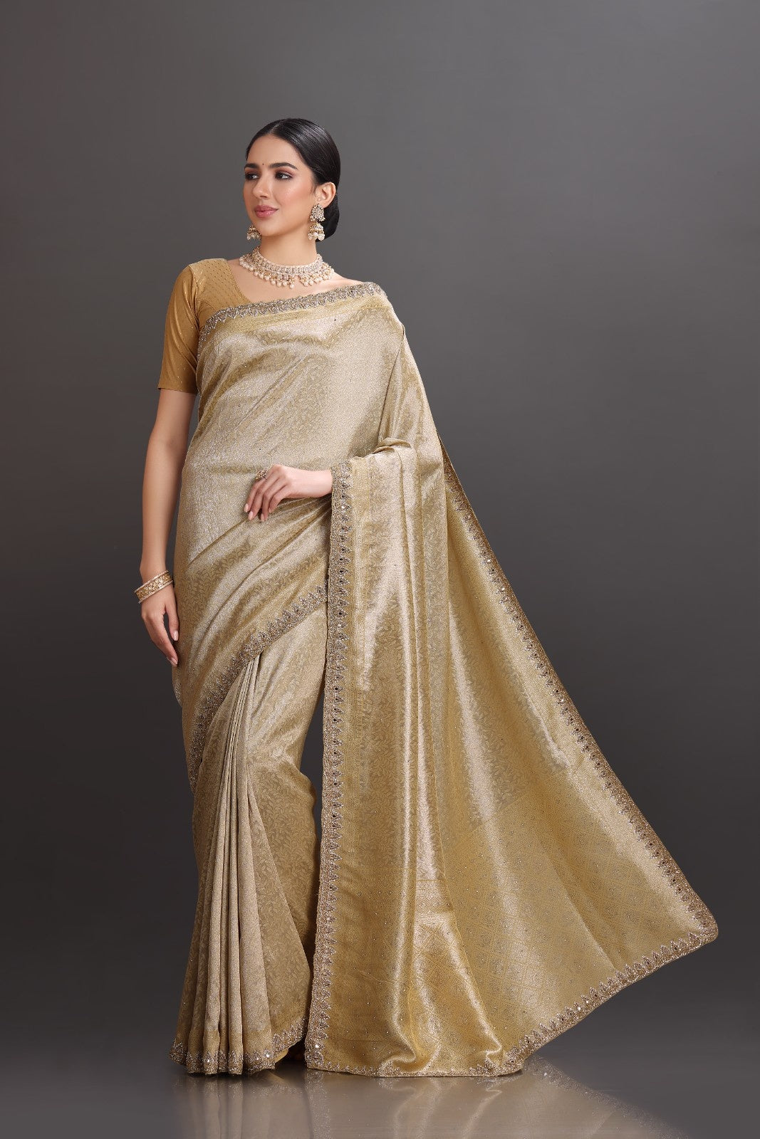 Woman wearing a gold saree with a plain background
