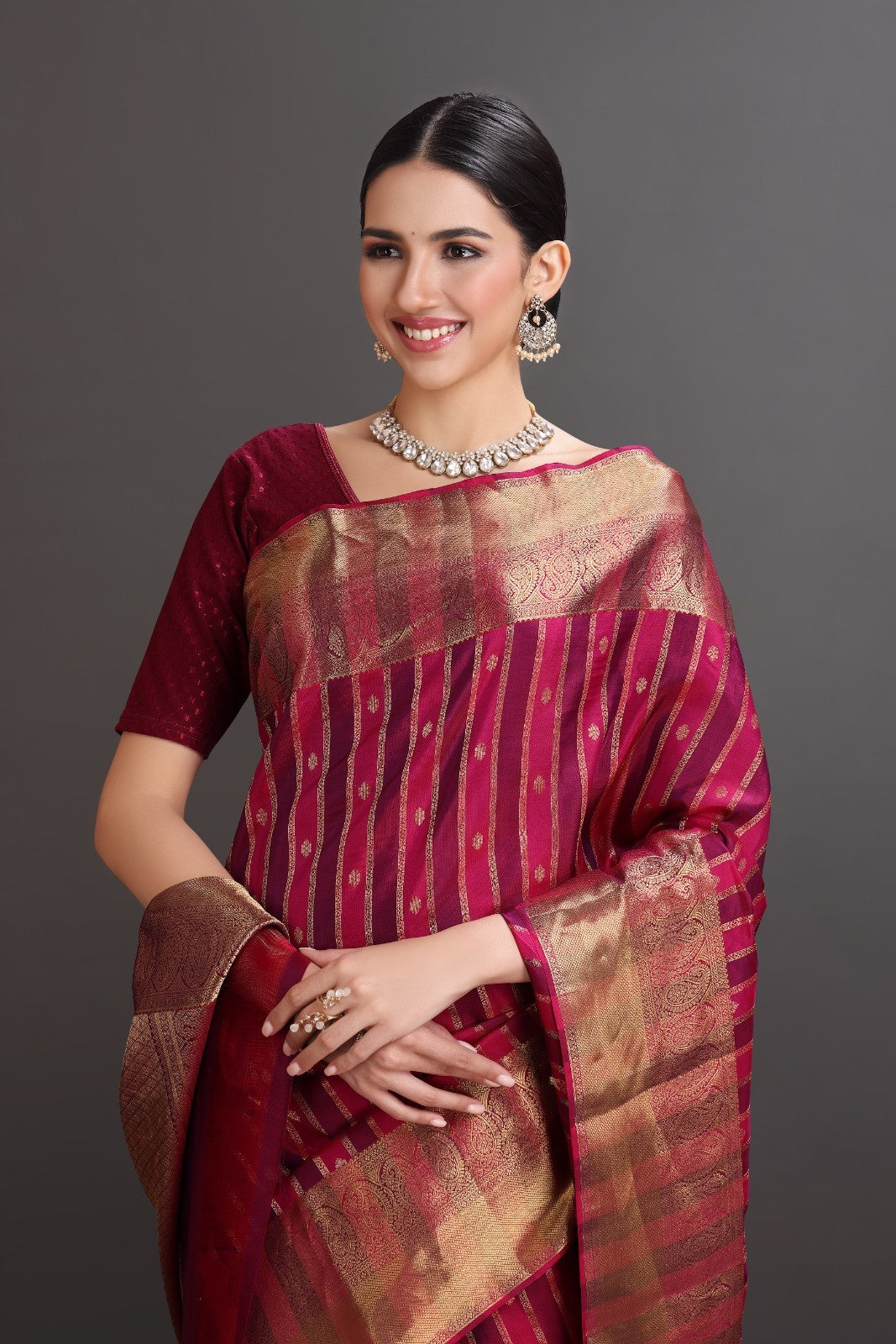Woman wearing a traditional maroon and gold saree with a plain background