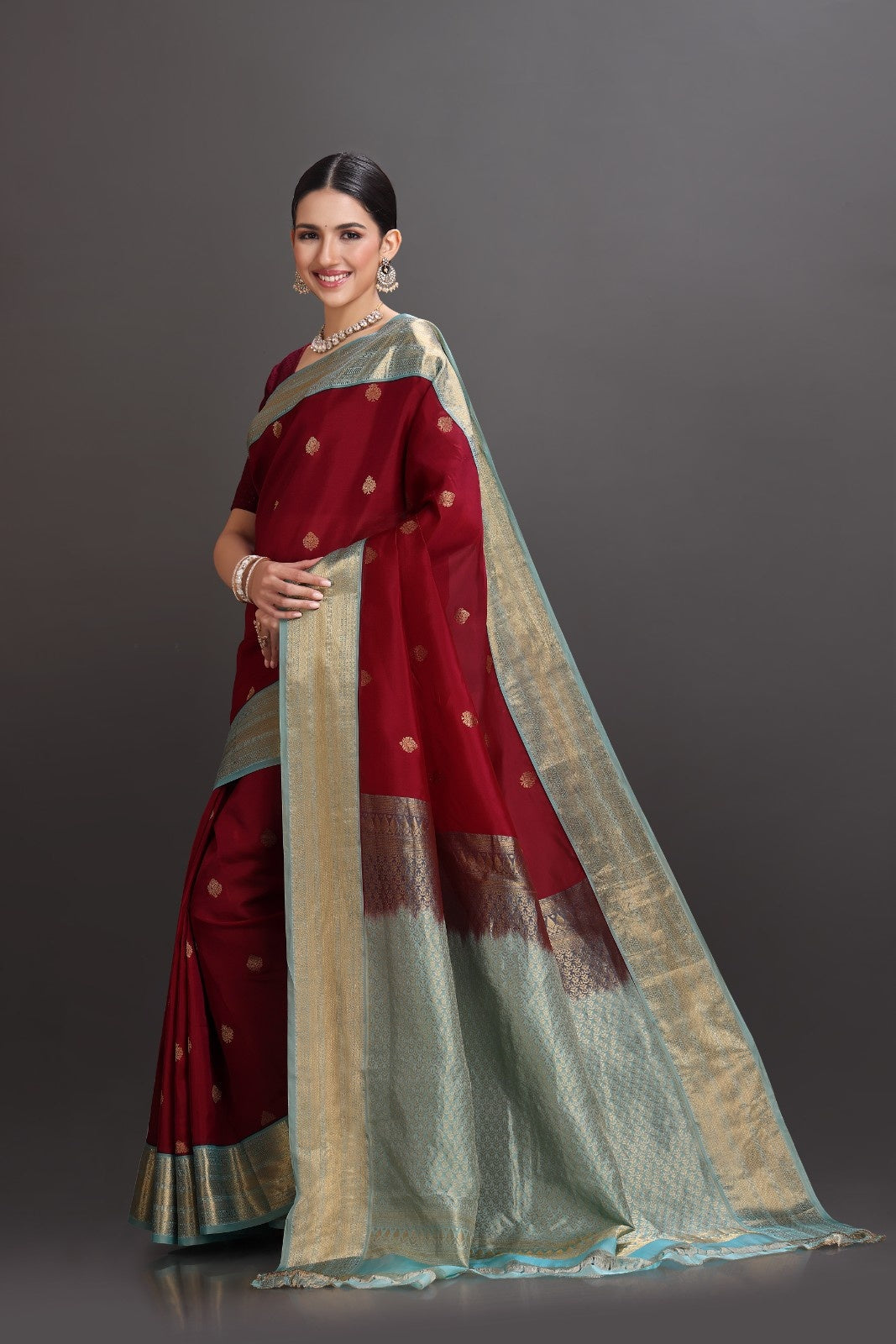 Woman wearing a traditional maroon and beige saree against a gray background