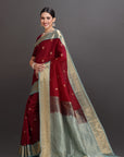 Woman wearing a traditional maroon and beige saree against a gray background