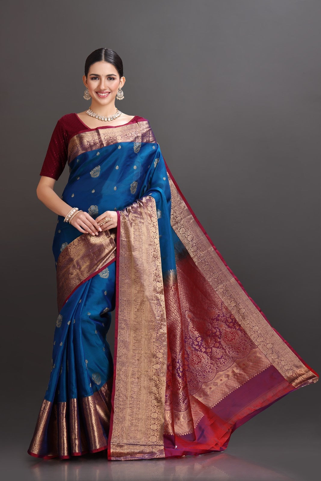 Woman wearing a traditional blue and red saree with a gold border on a gray background