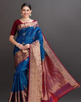 Woman wearing a traditional blue and red saree with a gold border on a gray background