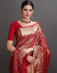 Woman wearing a red and gold saree with jewelry against a gray background