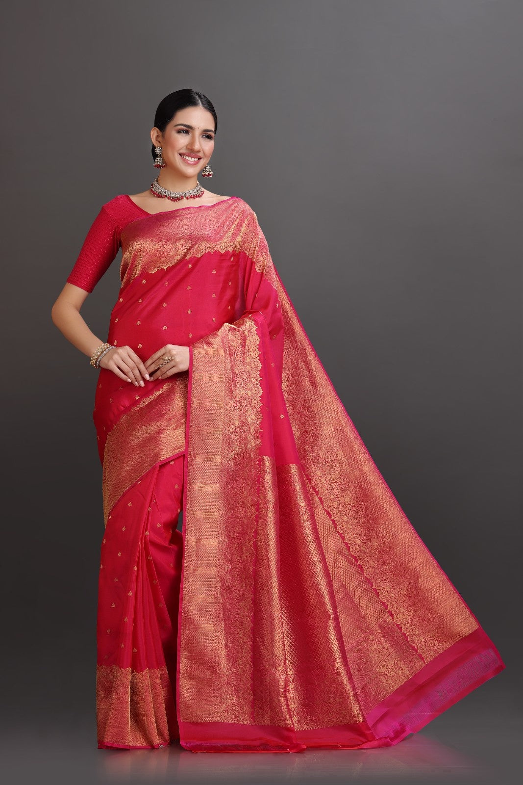 Woman wearing a red saree with a gold border on a gray background