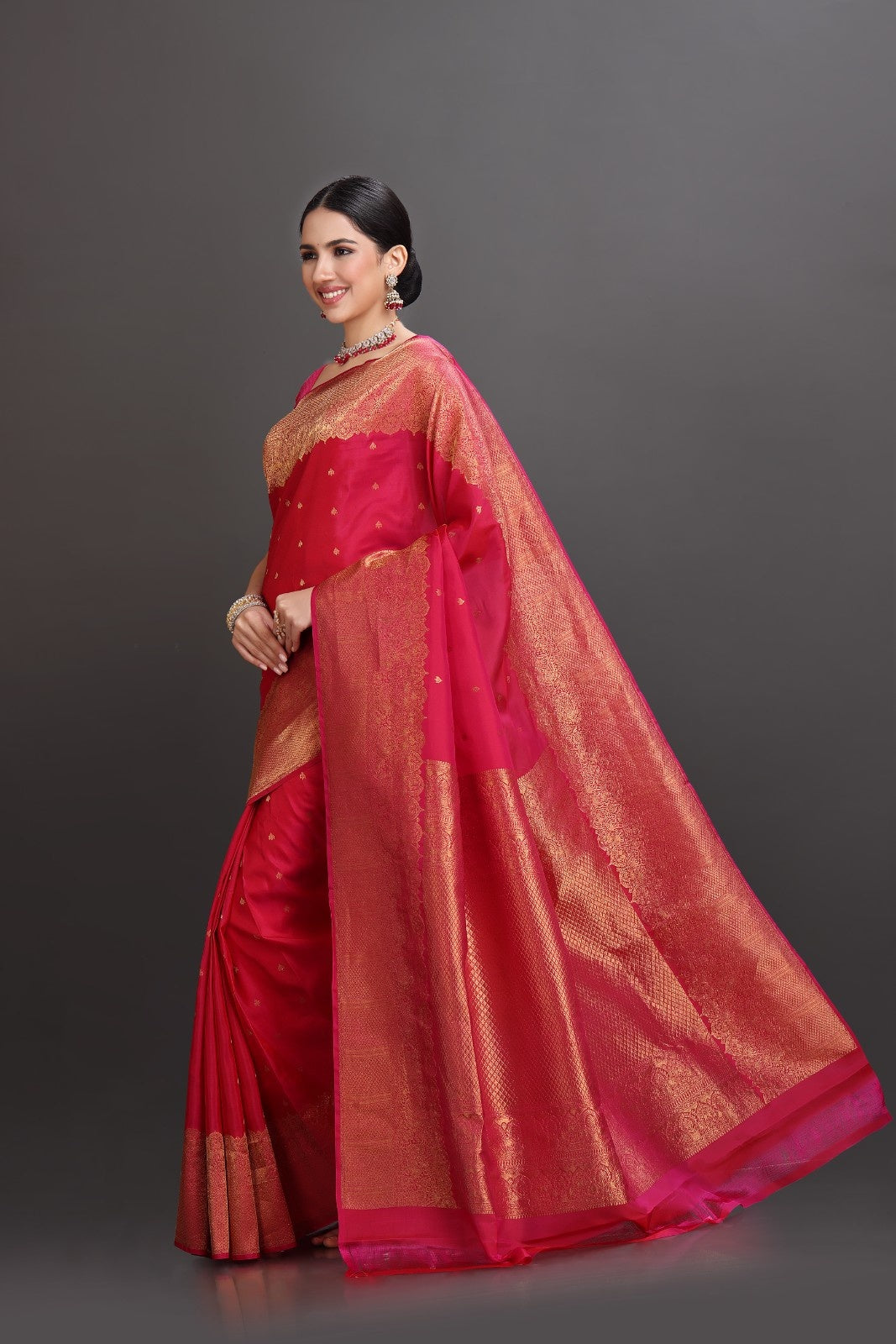 Woman wearing a red saree with a gold border on a gray background
