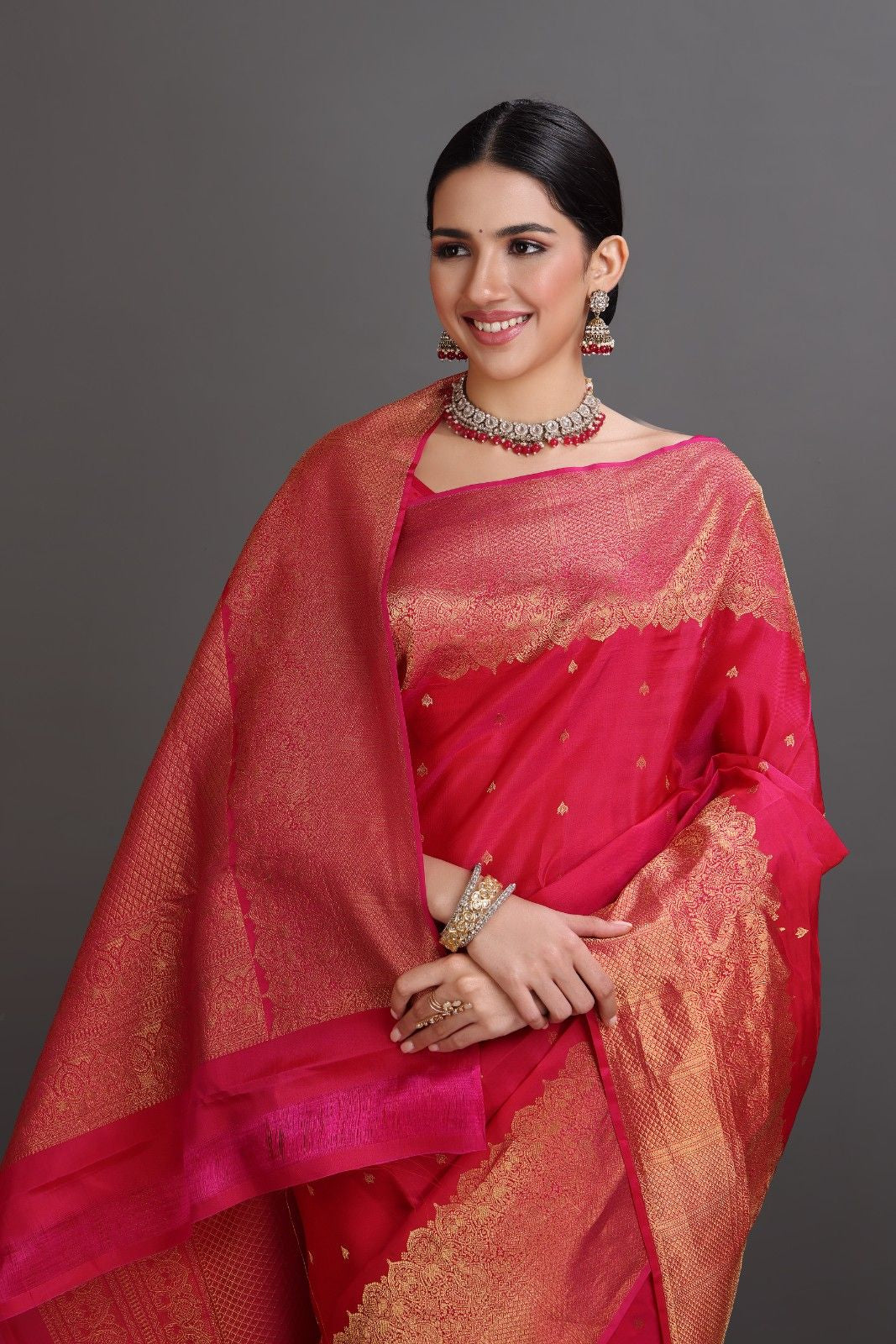 Woman wearing a red saree with gold patterns on a gray background
