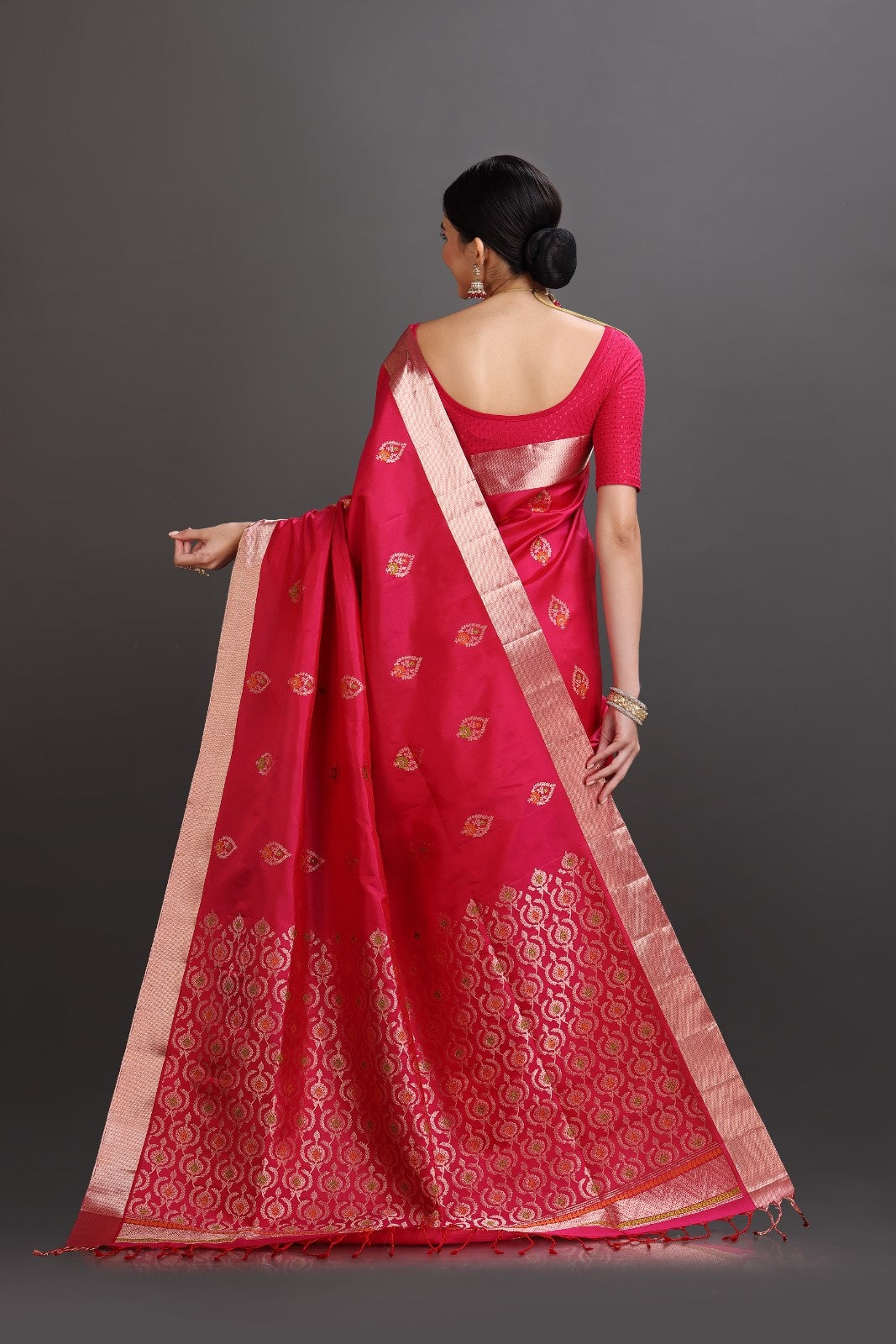 Woman wearing a red saree with a gold border on a gray background