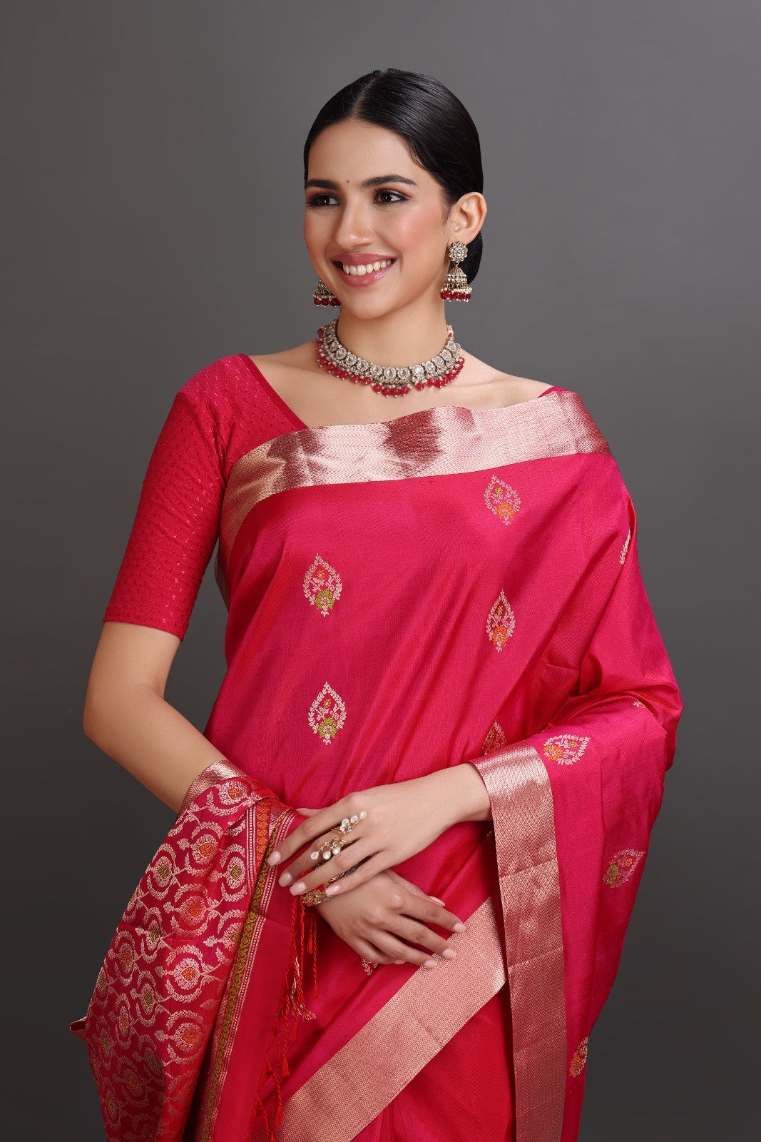 Woman wearing a traditional red saree with gold patterns on a gray background